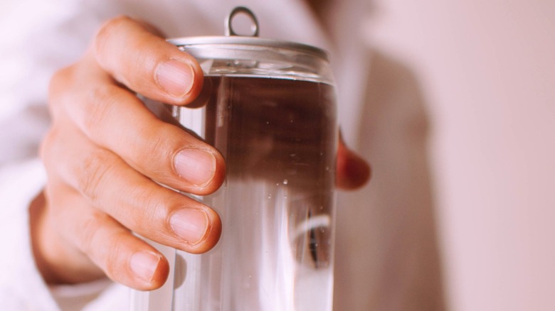Hand holding a clear soda can filled with liquid