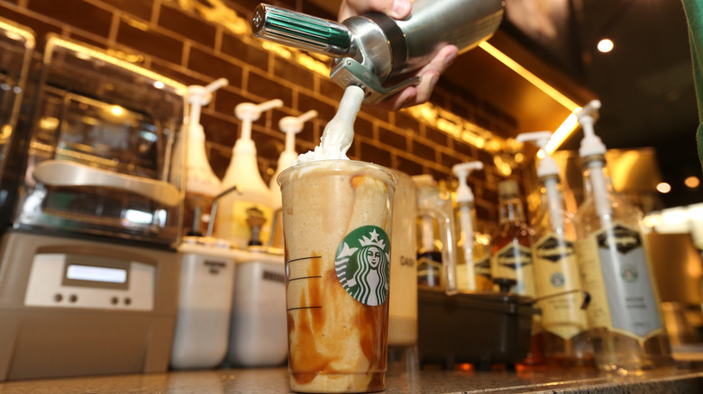 Whipped cream being added to the top of a Starbucks iced drink.
