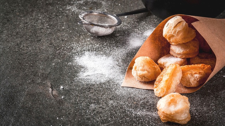 Small croissant donuts in a paper cone with powdered sugar on a grey surface