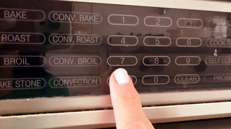 Finger touching buttons on oven