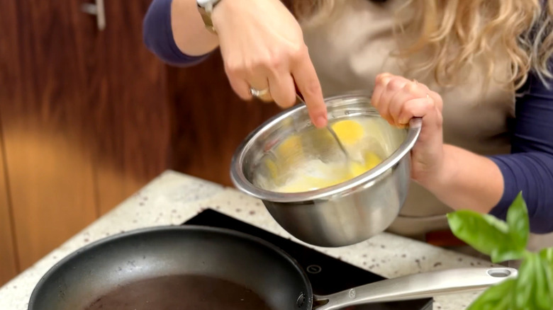 Person whisking eggs with fork in metal bowl