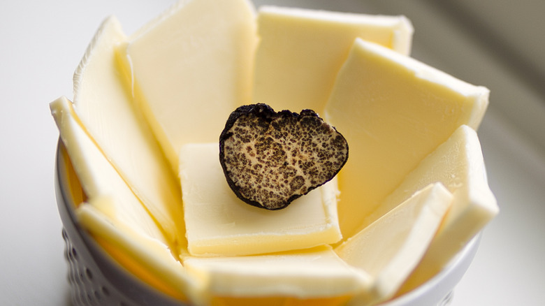 Half a black truffle sitting on top of butter slices in a white ramekin