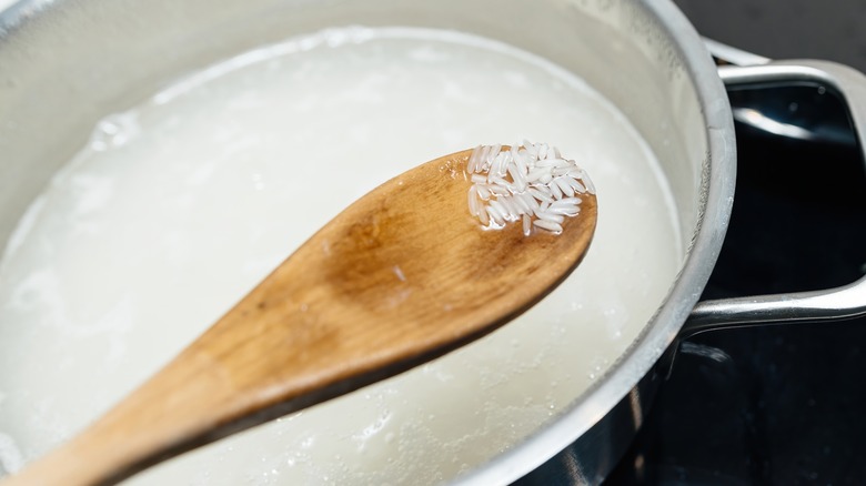 basmati rice in wooden spoon over pot of water 